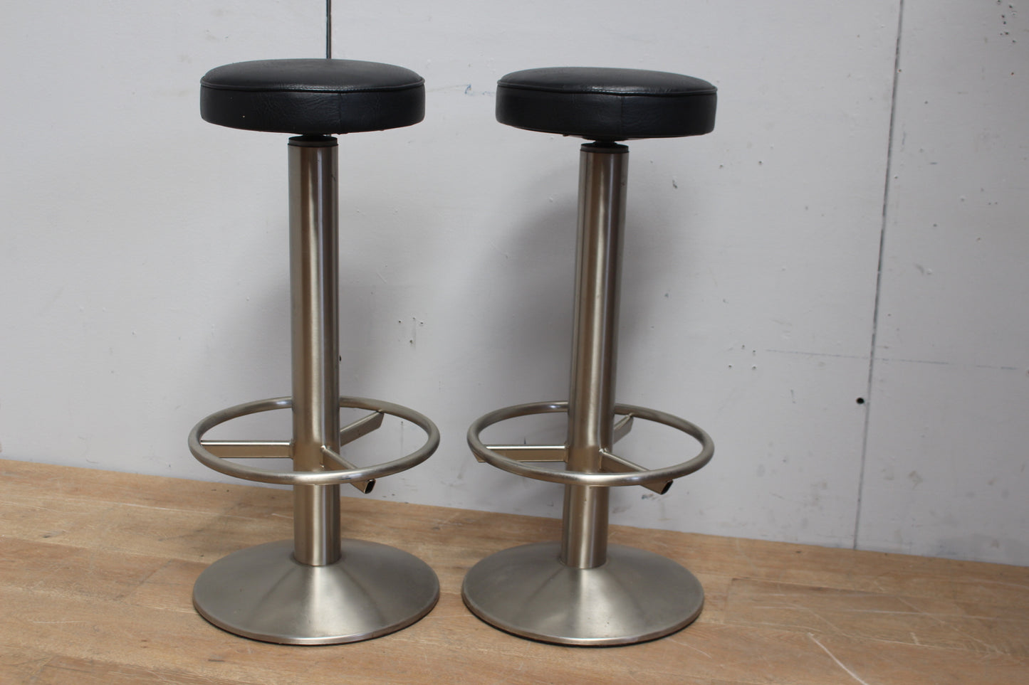 Pair of stainless steel bar stools with leather upholstered swivelled seats