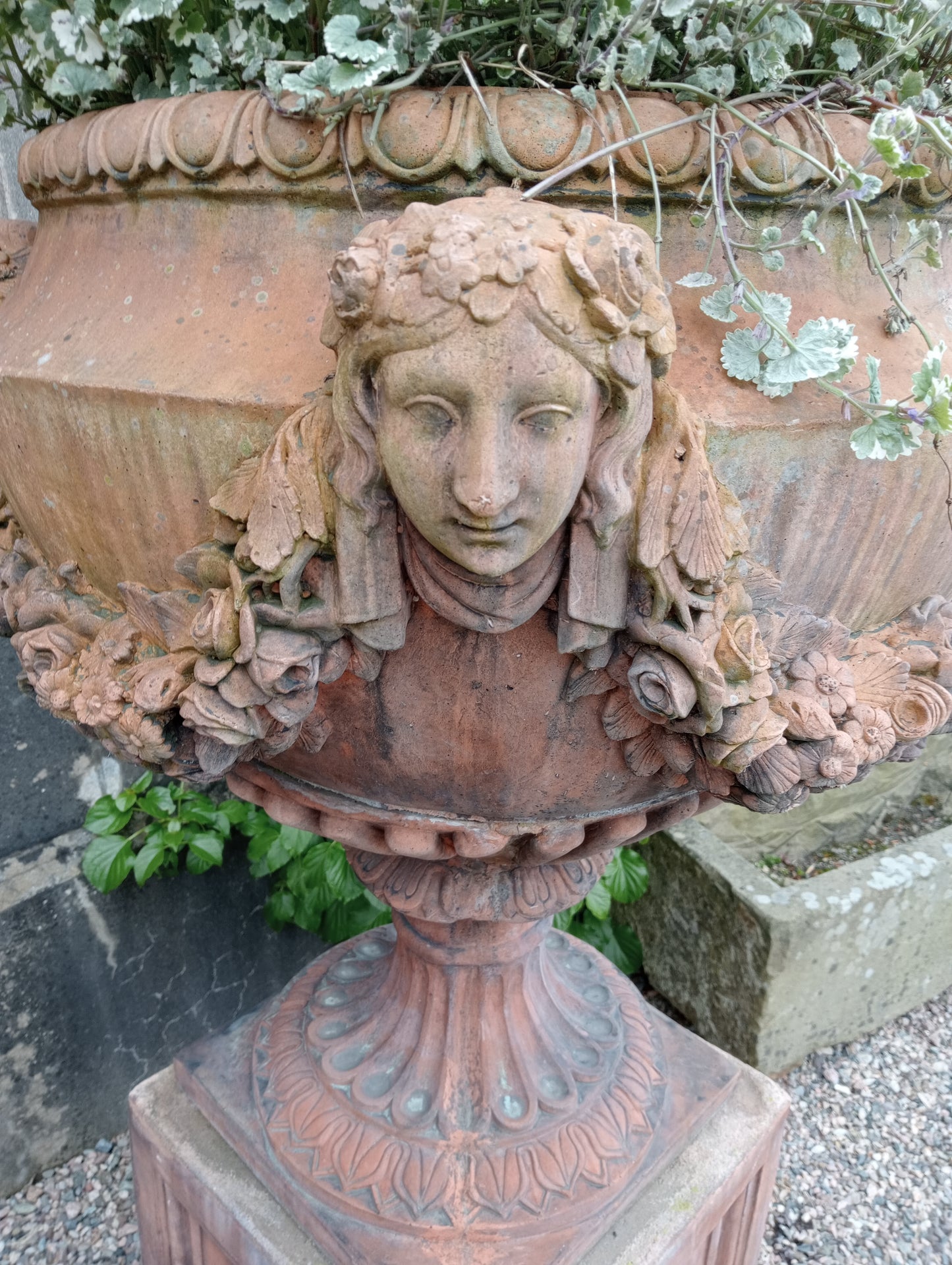 Pair of terracotta urns and bases depicting swags and faces