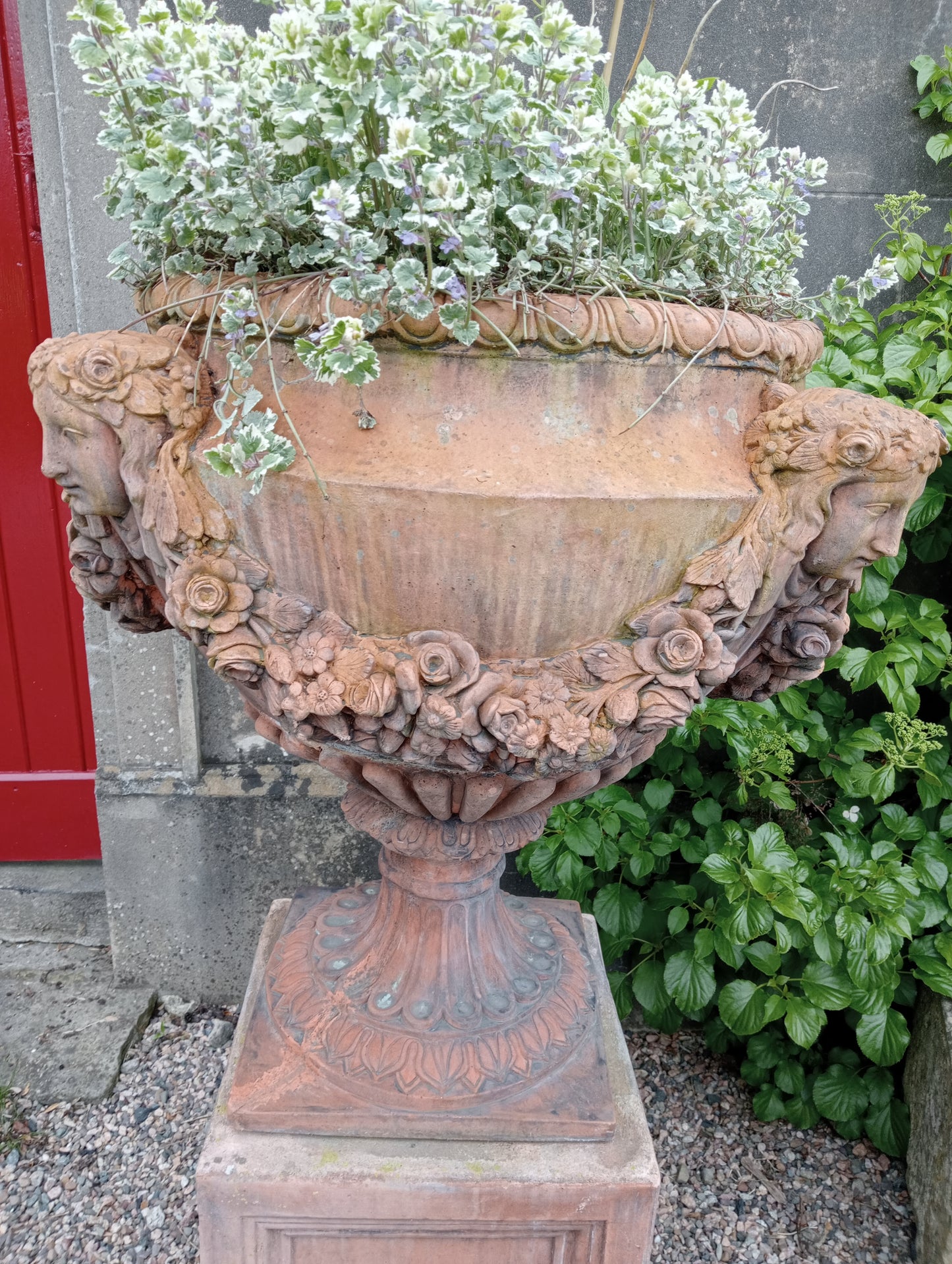 Pair of terracotta urns and bases depicting swags and faces