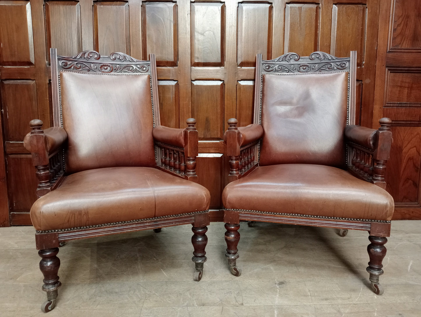 Pair of oak fireside chairs with tan leather on turned front legs with castors