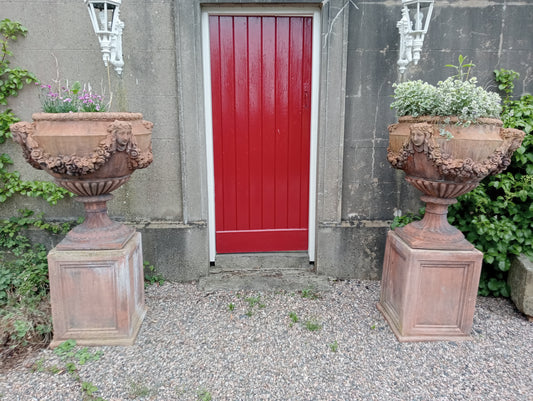 Pair of terracotta urns and bases depicting swags and faces